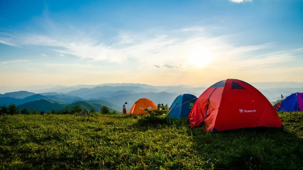 Colorful tents set up on a grassy mountain ridge during a wild camping trip at sunset